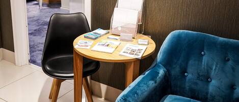 A hotel room with a blue armchair, a wooden table with brochures, and a decorative wall piece.