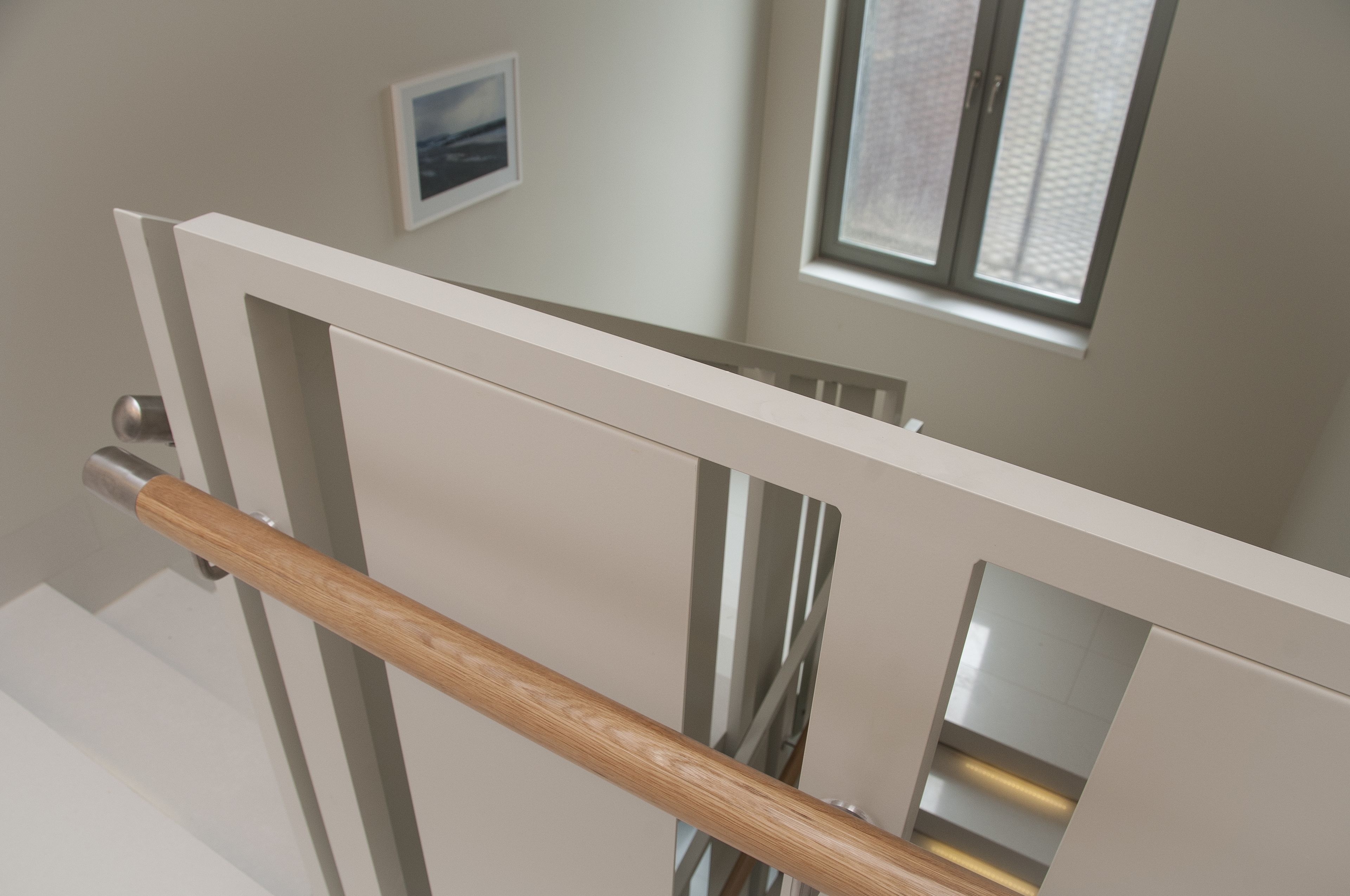 Una escalera moderna con barandilla de madera, una puerta blanca y un ventanal con persianas.