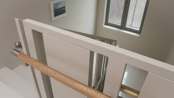 Una escalera moderna con barandilla de madera, una puerta blanca y un ventanal con persianas.