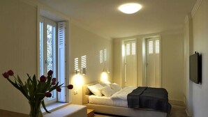 A bedroom with a bed, bedside tables, a vase of flowers, and a window with shutters. - Baltica Residence (Sopot)