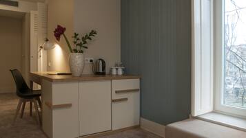 A small kitchenette with a wooden countertop, a white cabinet, a vase with a red rose, a kettle, and a coffee maker.