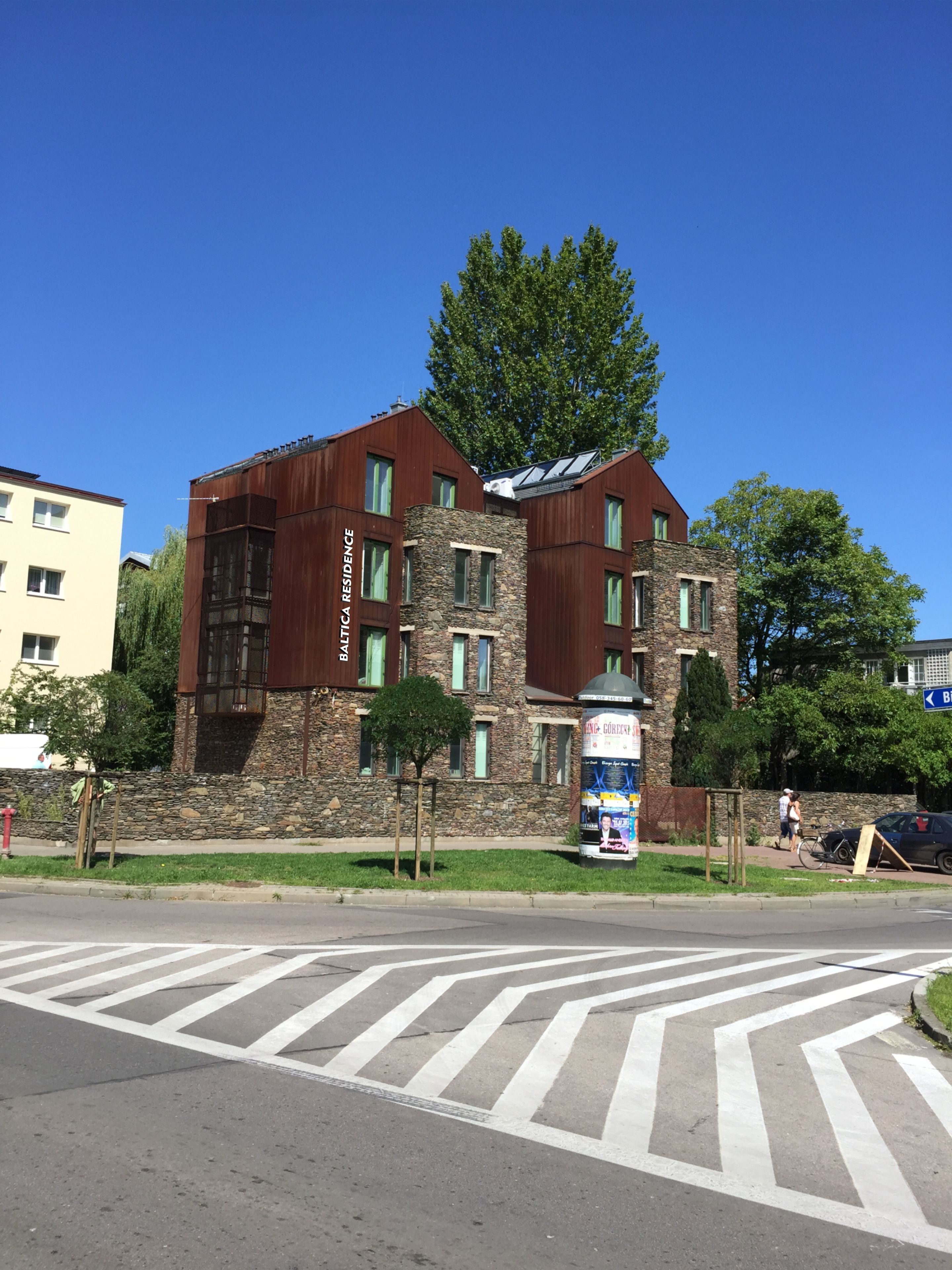 A modern building with a stone facade and a large tree in front.