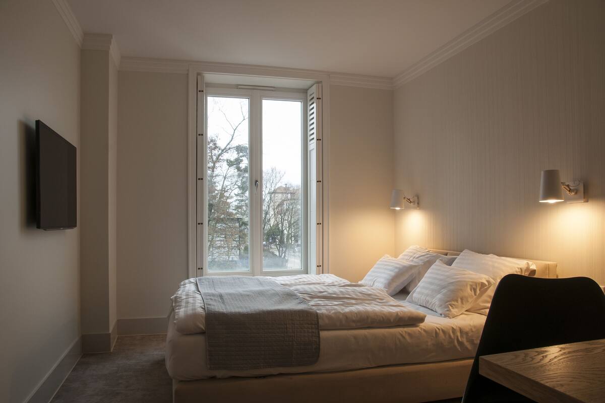 Un dormitorio con una cama, una silla, un televisor y una ventana con persianas.