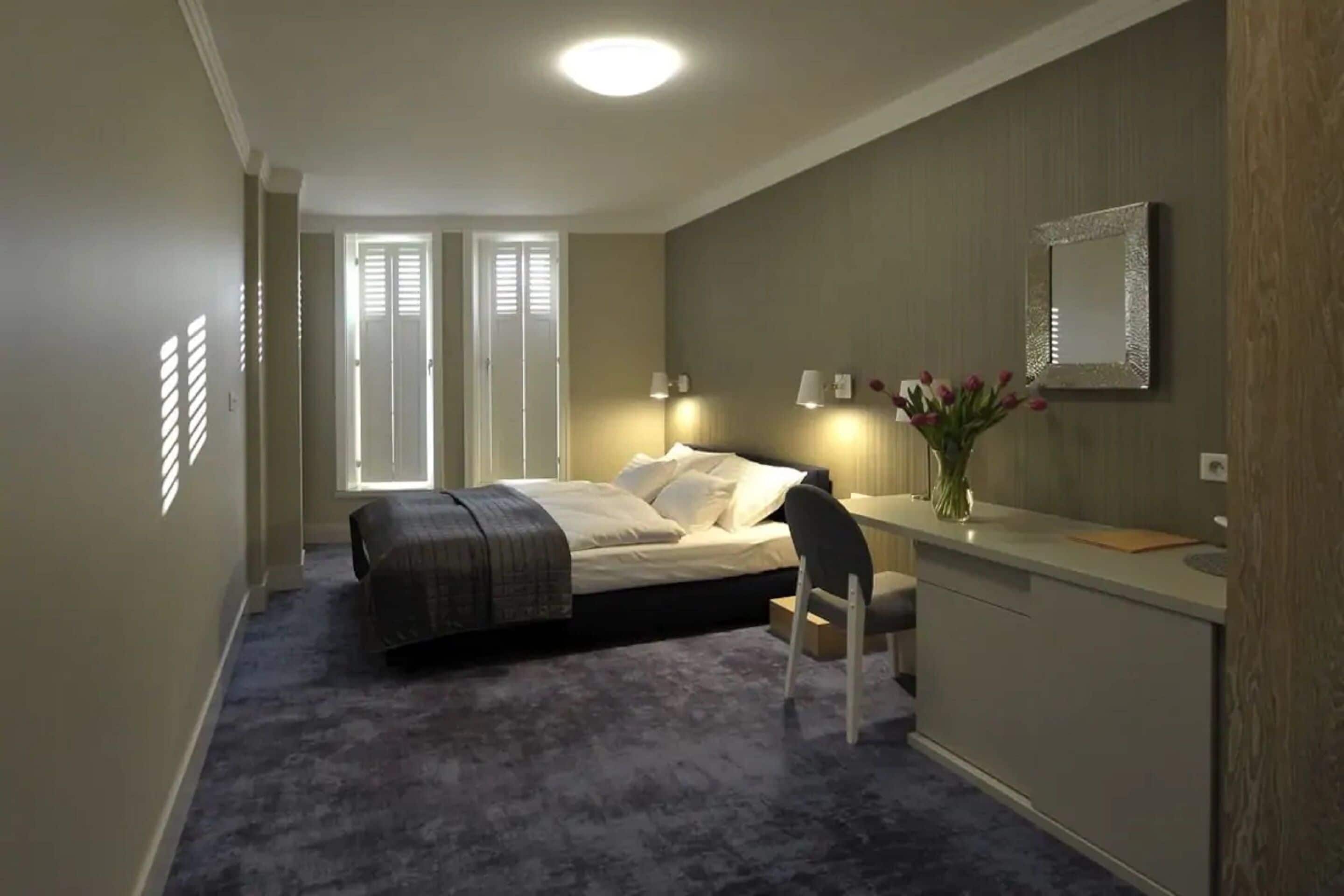A bedroom with a bed, bedside table, chair, and a desk with a mirror.