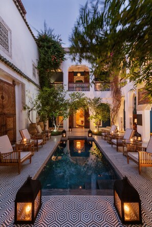 A courtyard with a pool, wooden furniture, and lanterns. - Riad Les Yeux Bleus (Marrakech)