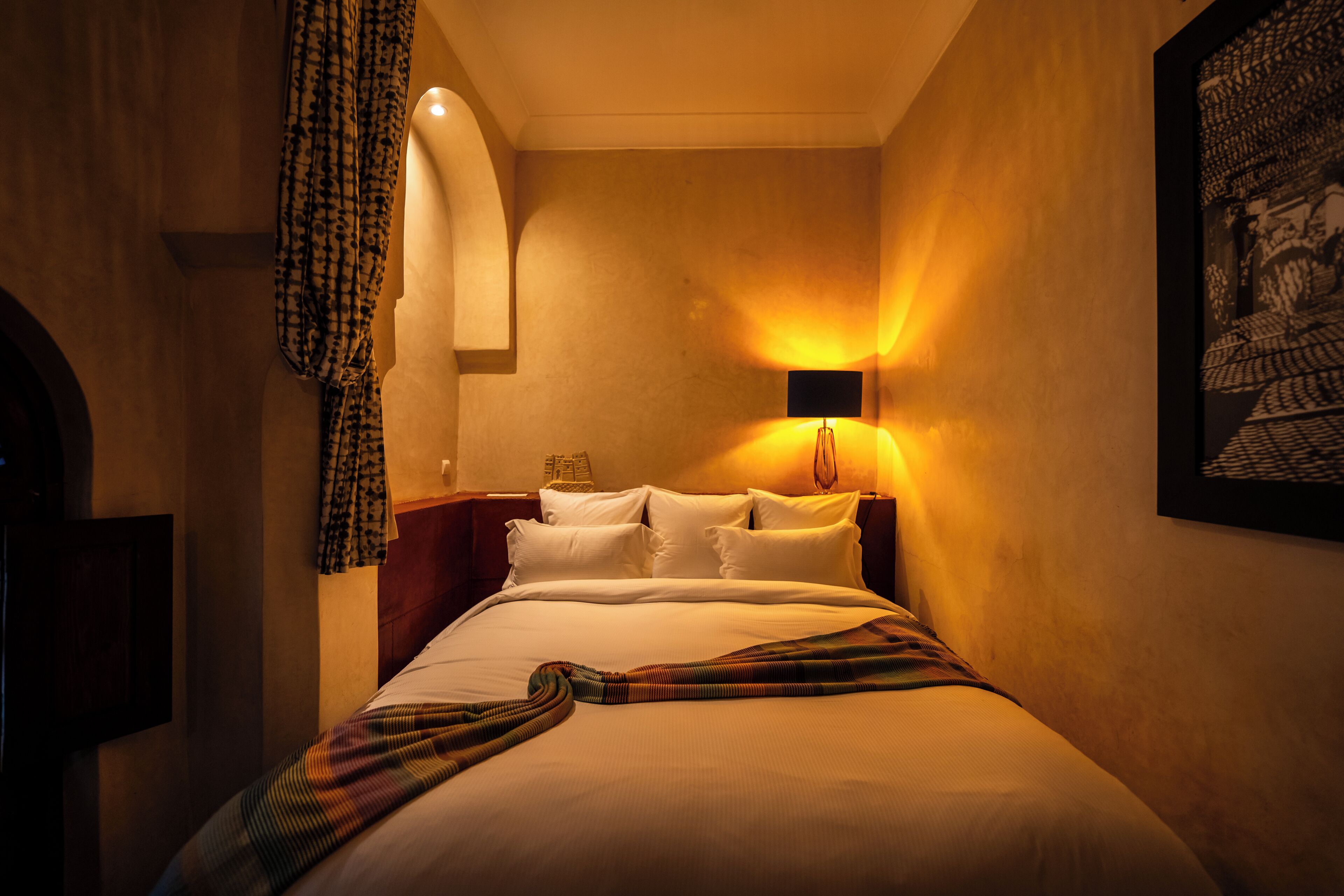 Una habitación de hotel con cama, cabecera, lámpara de pared y un cuadro enmarcado.