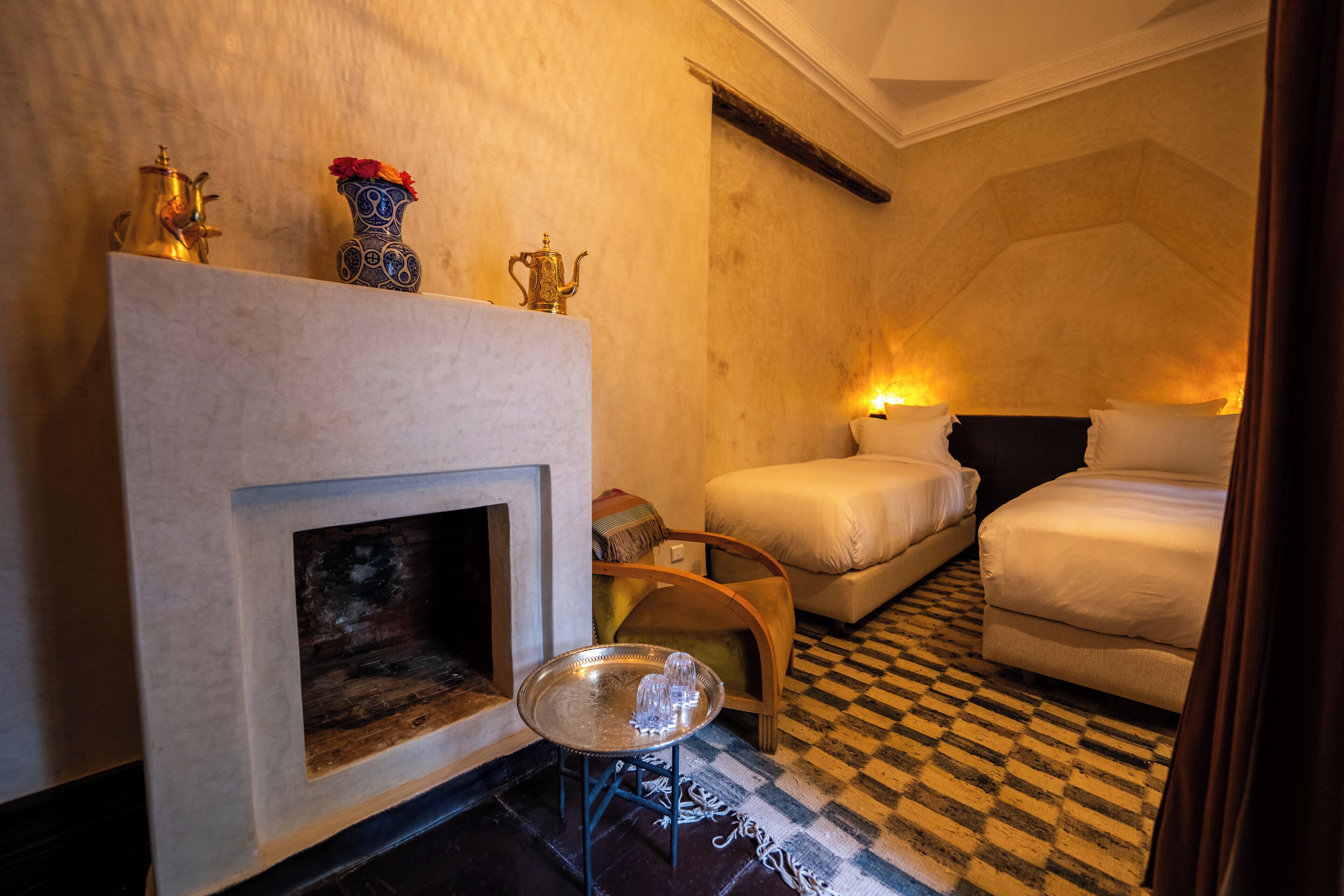 A hotel room with a fireplace, two beds, a checkered floor, and decorative items on the mantel.