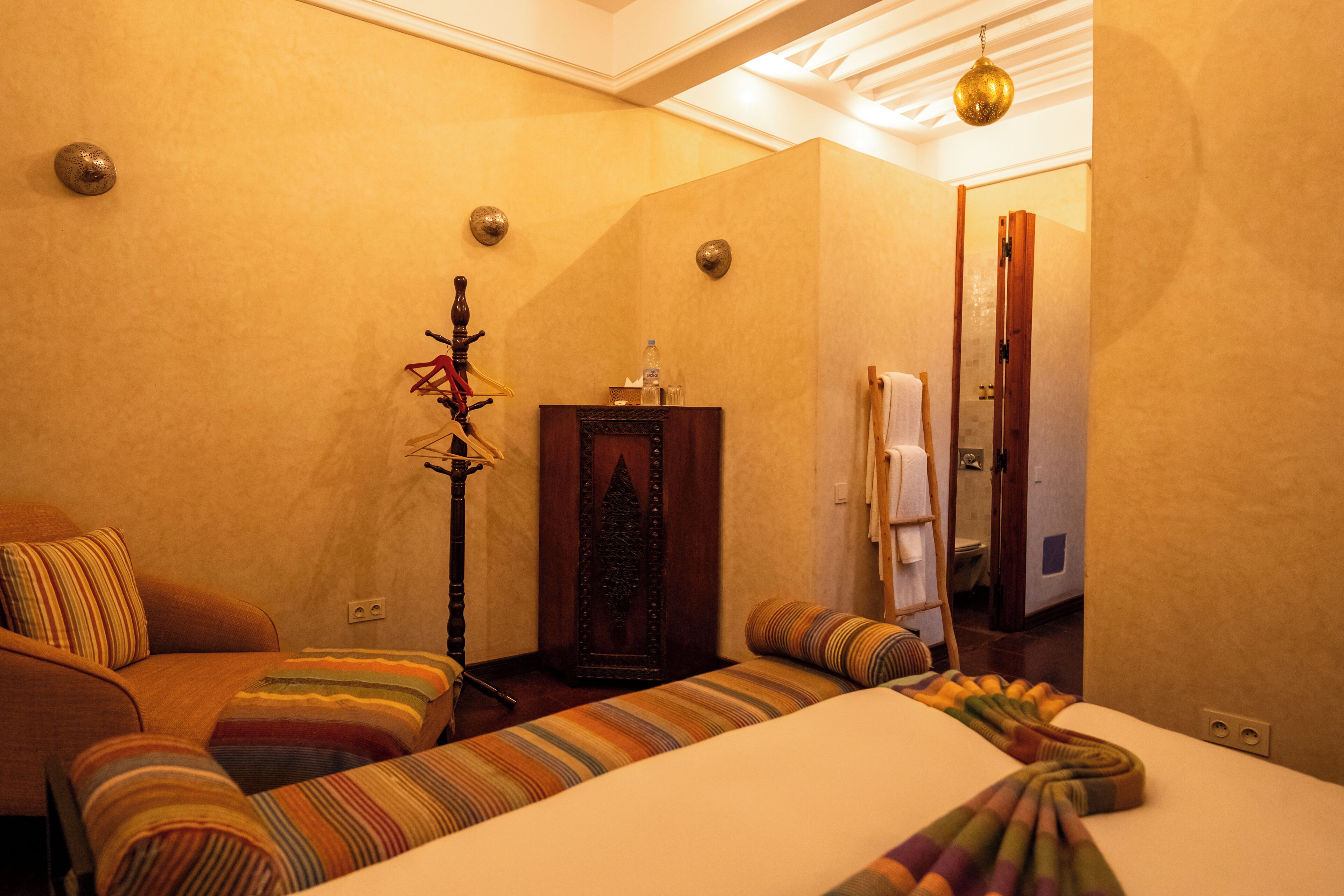 A hotel room with a bed, a sofa, a wooden cabinet, and a mirror.