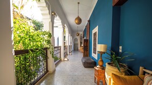 Un couloir doté d’un sol à motifs, d’un mur bleu et d’un balcon agrémenté de plantes.