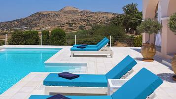 Zona de piscina con sillones de descanso y vistas a un paisaje montañoso.