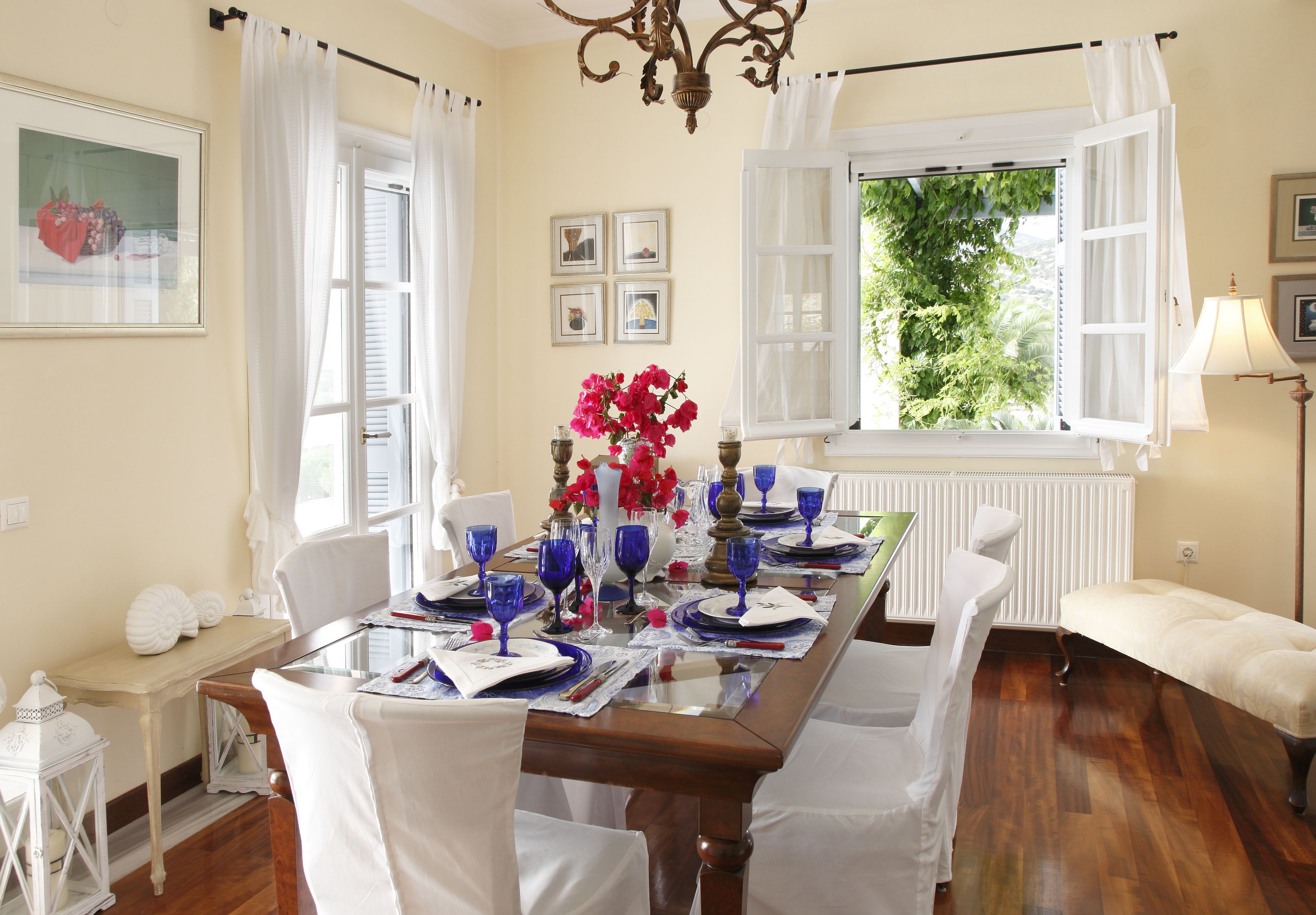 A dining room with a wooden table set for a meal, white chairs, and a view of greenery outside.