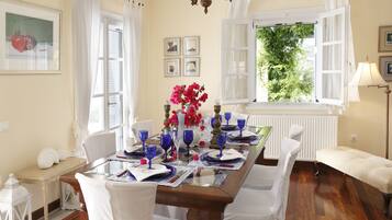 A dining room with a wooden table set for a meal, white chairs, and a view of greenery outside.