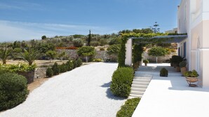 A white building with a stone wall and a gravel driveway leading to a white porch.