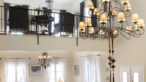 A spacious living room with a high ceiling, a chandelier, and a dining area with a table and chairs.