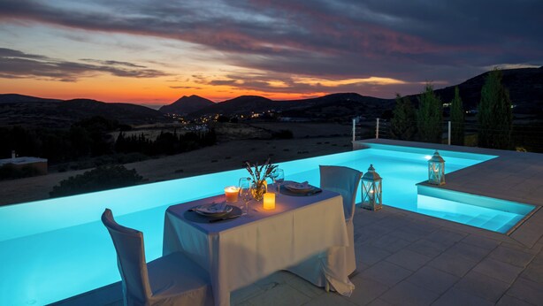 An outdoor dining area with a table set for two, overlooking a mountainous landscape during sunset.