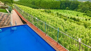 A swimming pool with a wooden deck and metal railing, surrounded by lush greenery and a view of distant hills. - Wellness Suite Na Canunà (Roddi)