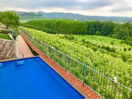 Piscina con cubierta de madera y barandilla de metal, rodeada de exuberante vegetación y vistas a colinas distantes.