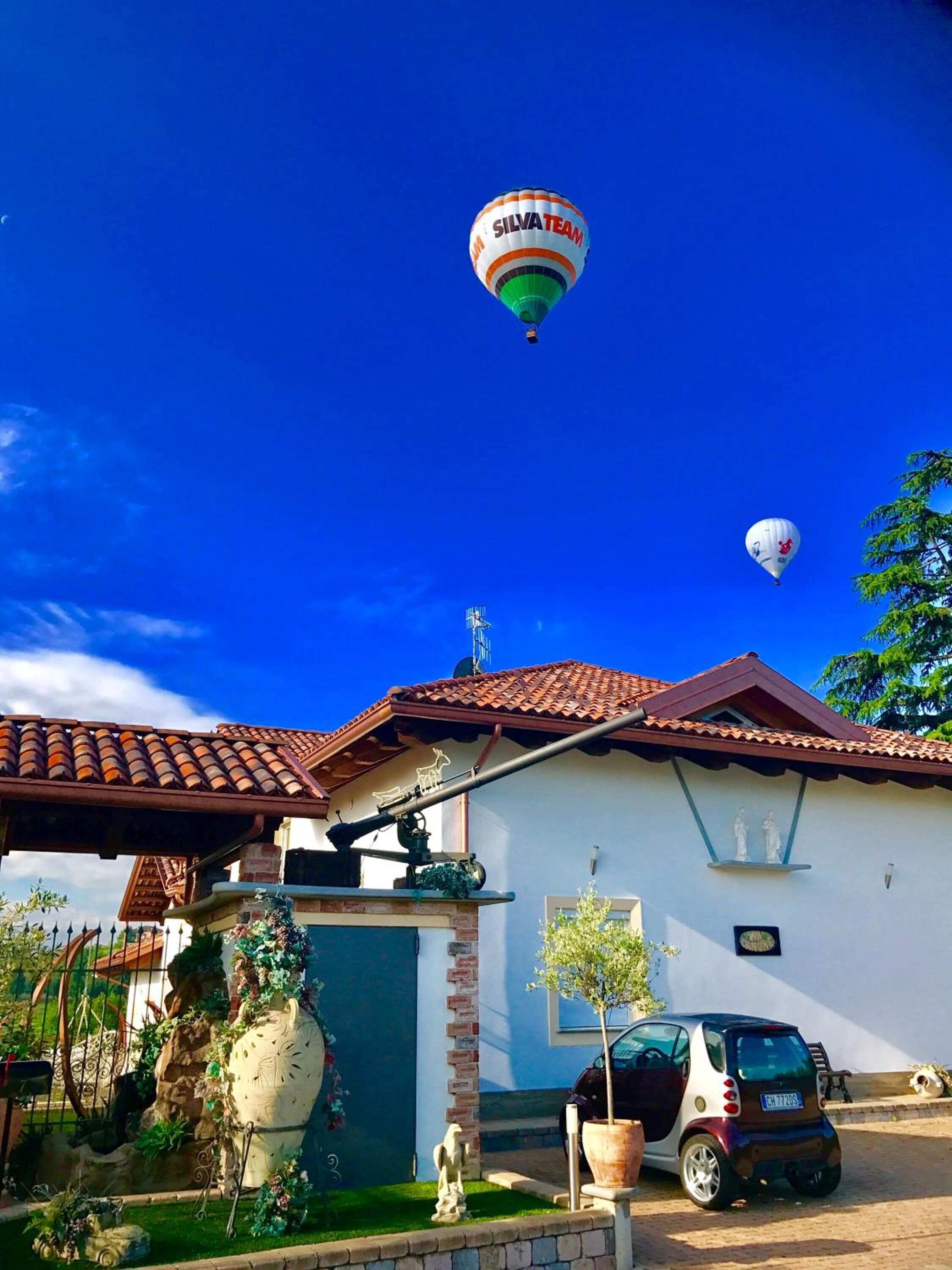 A house with a tiled roof, a small car, and a hot air balloon in the sky.