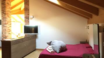 A bedroom with a bed, a TV, a dresser, and a brick wall.