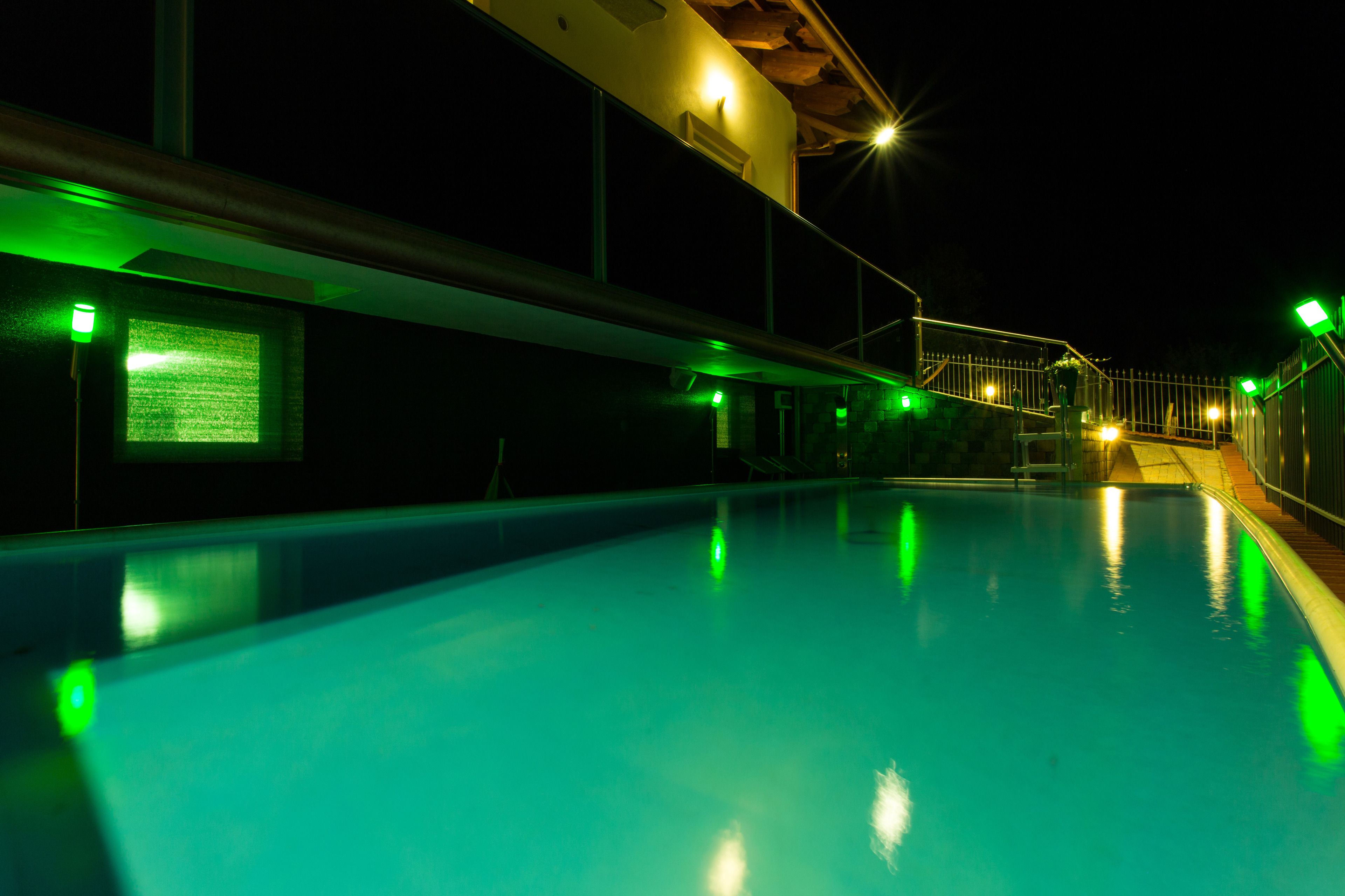 Ein Swimmingpool mit einer grün beleuchteten Außenfassade und einer Treppe zu einem überdachten Bereich.