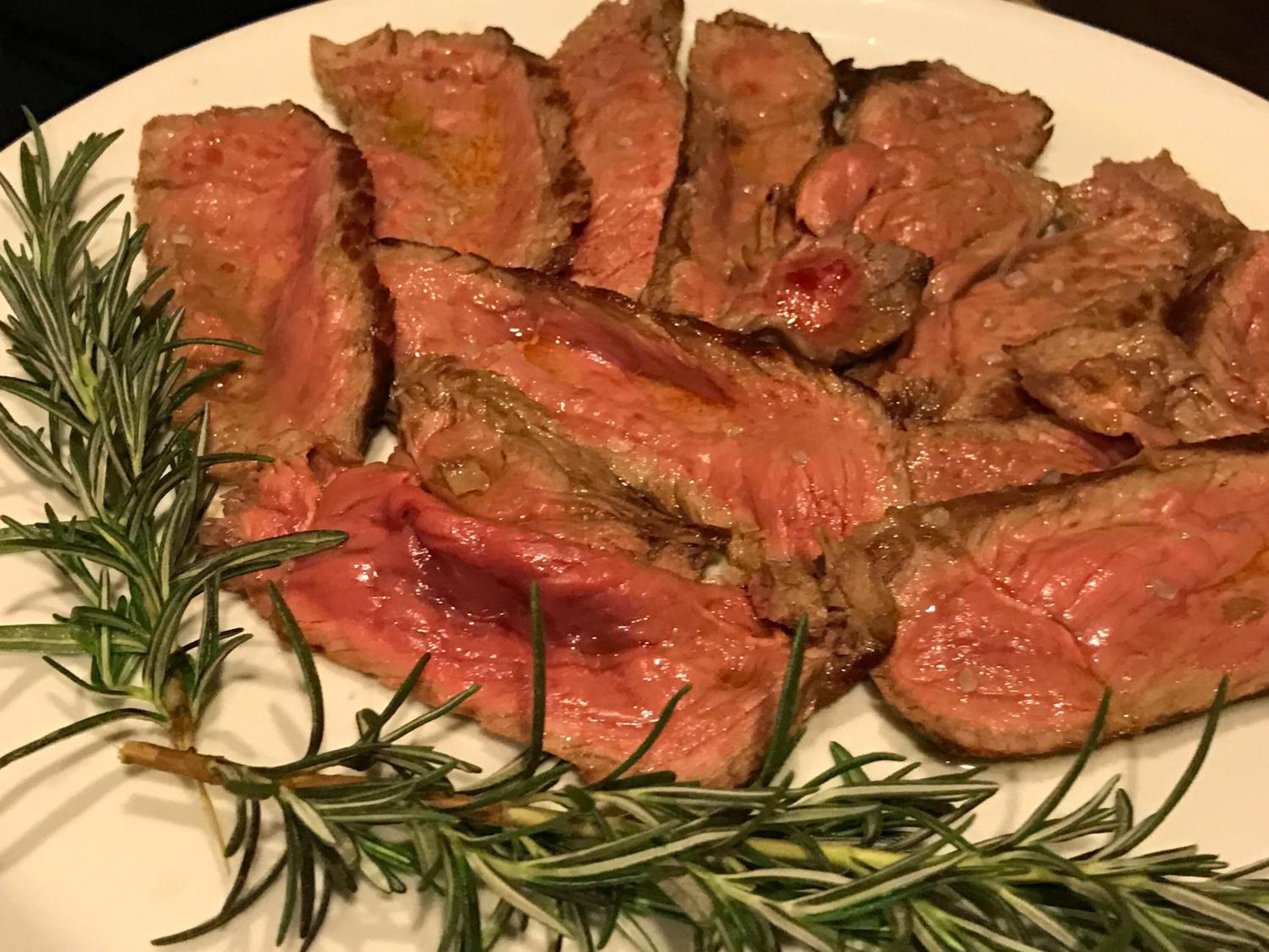A plate of sliced steak garnished with rosemary.