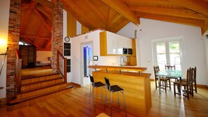 A spacious kitchen with a central island, wooden flooring, and a staircase leading to an upper level. - Wellness Suite Na Canunà (Roddi)