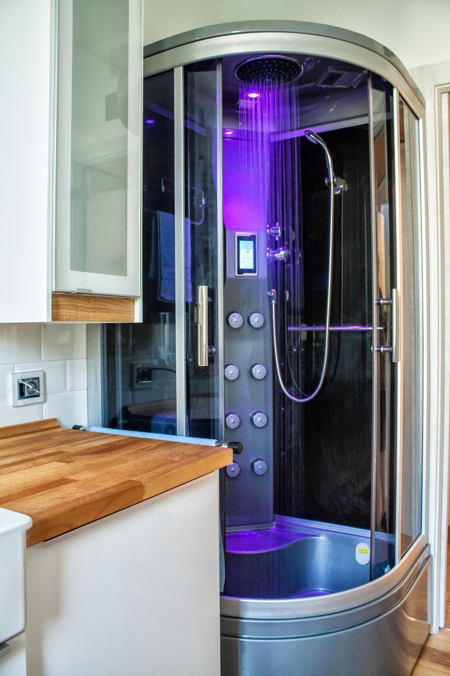 Un bagno moderno con cabina doccia in vetro, piano di lavoro in legno e pannello di controllo.