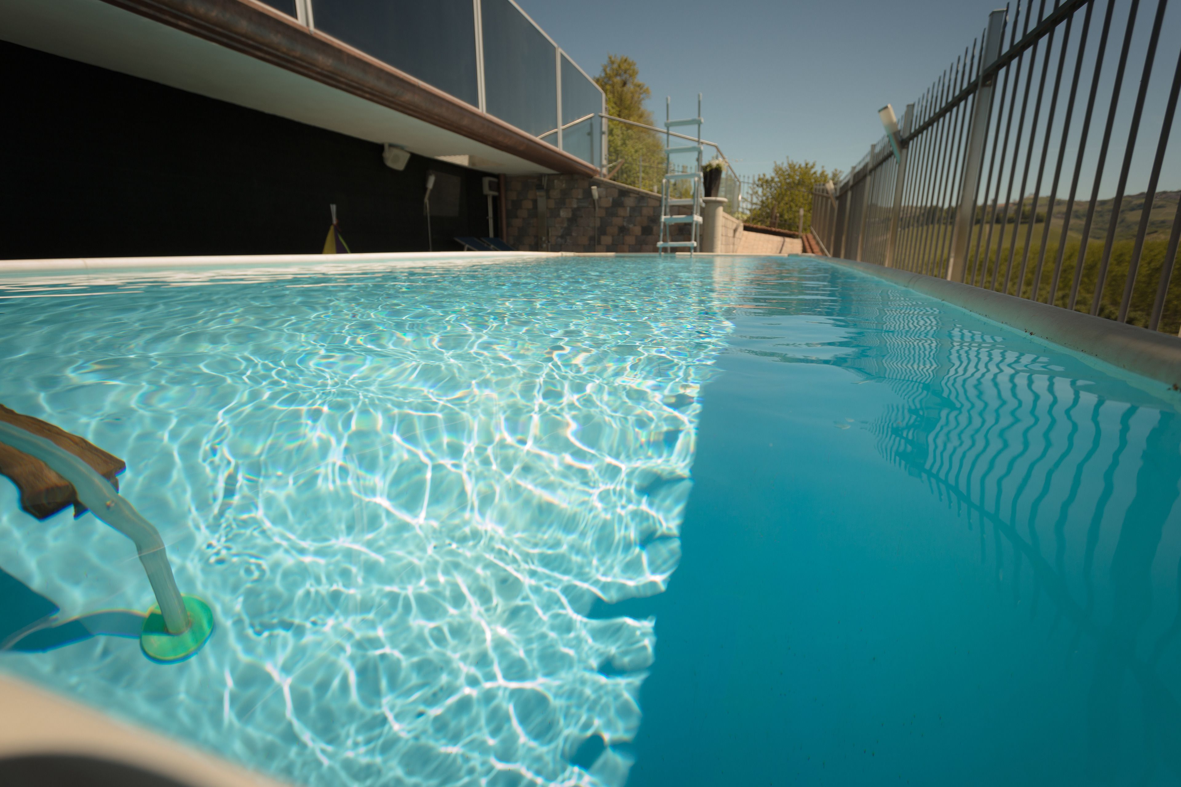 A clear swimming pool with a wooden deck and a metal fence.