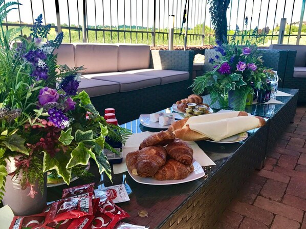Un área de estar al aire libre con una mesa dispuesta para el desayuno, incluyendo cruasanes, pastelería y salsas.