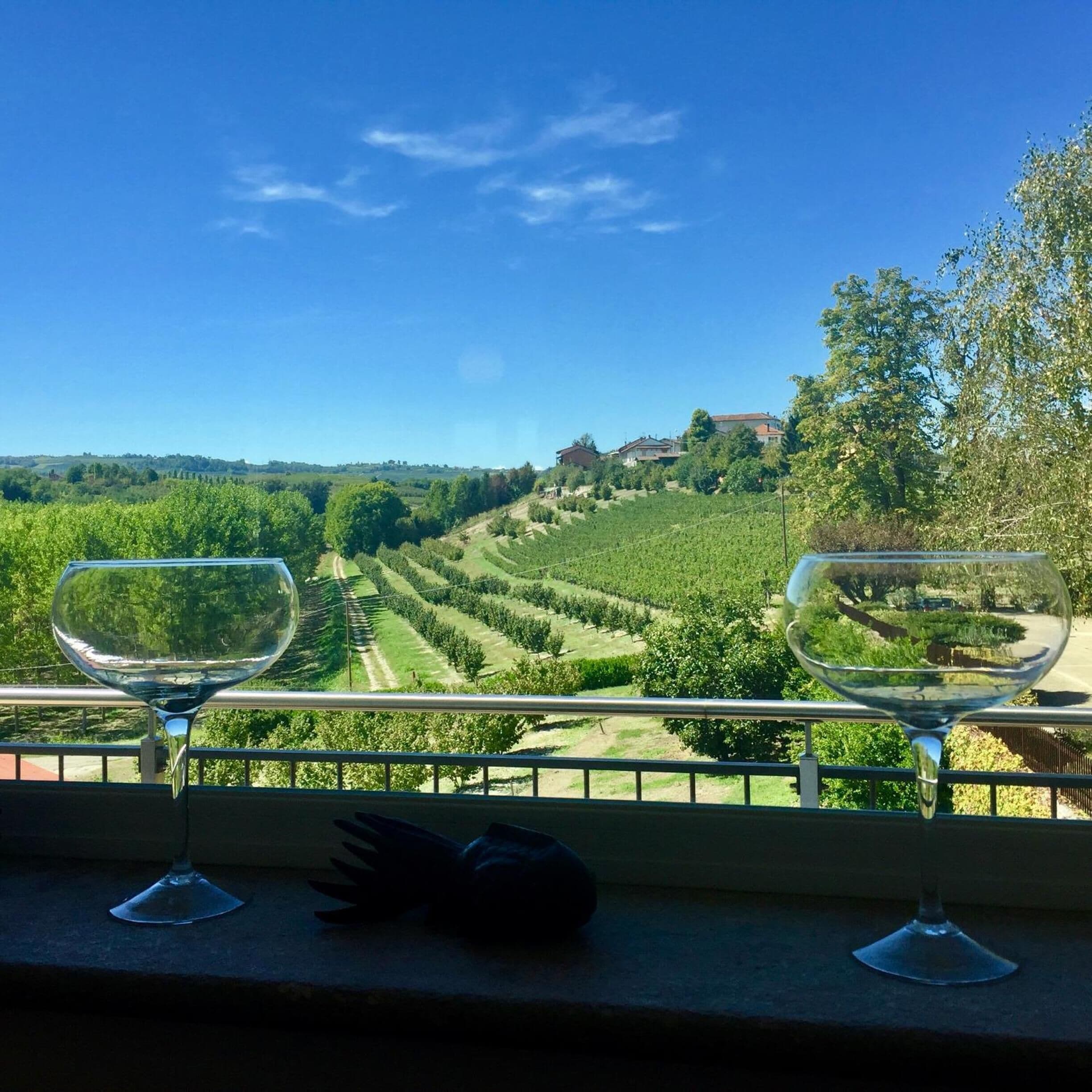 Balcón con dos copas de vino vacías con vista a un viñedo.