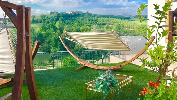 A backyard with a hammock, a table with flowers, and a view of the countryside with hot air balloons. - Wellness Suite Na Canunà (Roddi)
