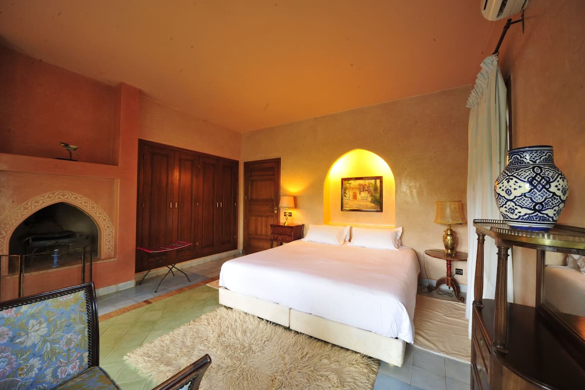 A bedroom with a large bed, a fireplace, wooden furniture, and a decorative vase.