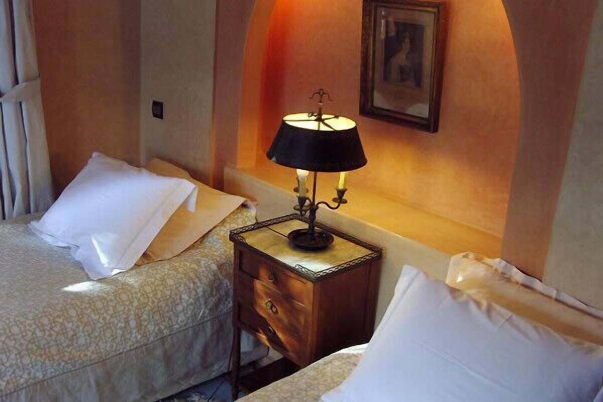 A hotel room with two beds, a nightstand with a lamp, and a framed picture on the wall.