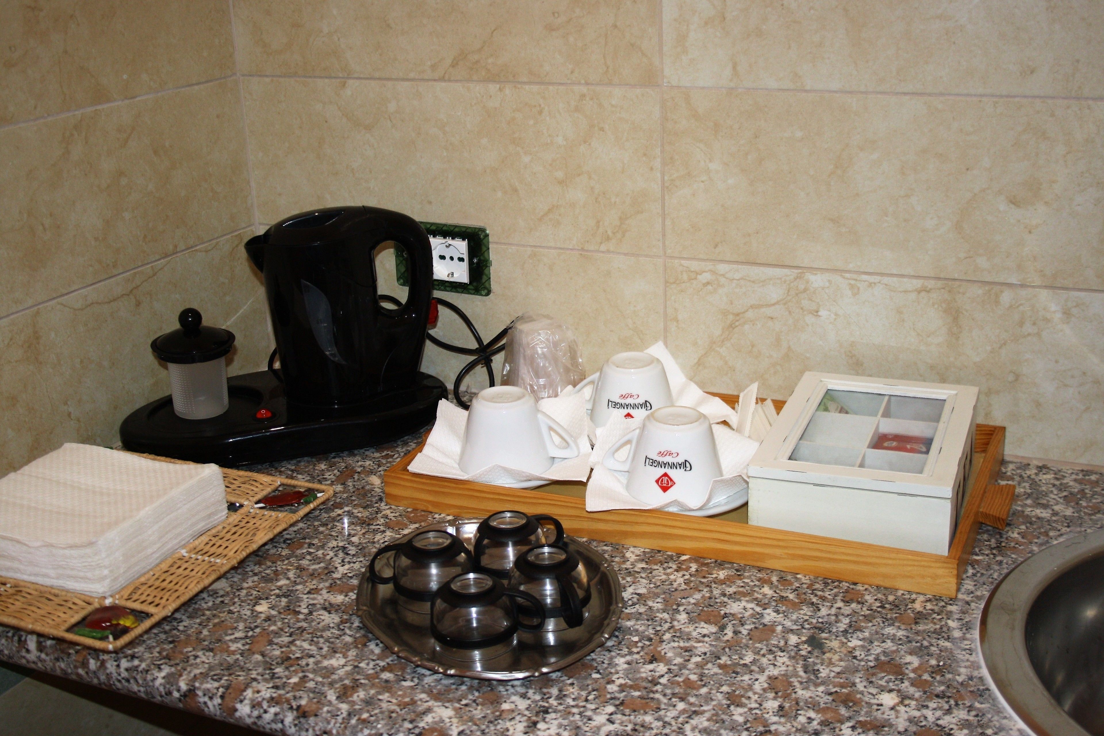 A kitchen counter with a coffee maker, tea kettle, cups, and a tray with a box.