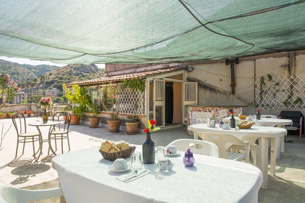 Un patio exterior con mesas y sillas, plantas en macetas y vistas a una colina.