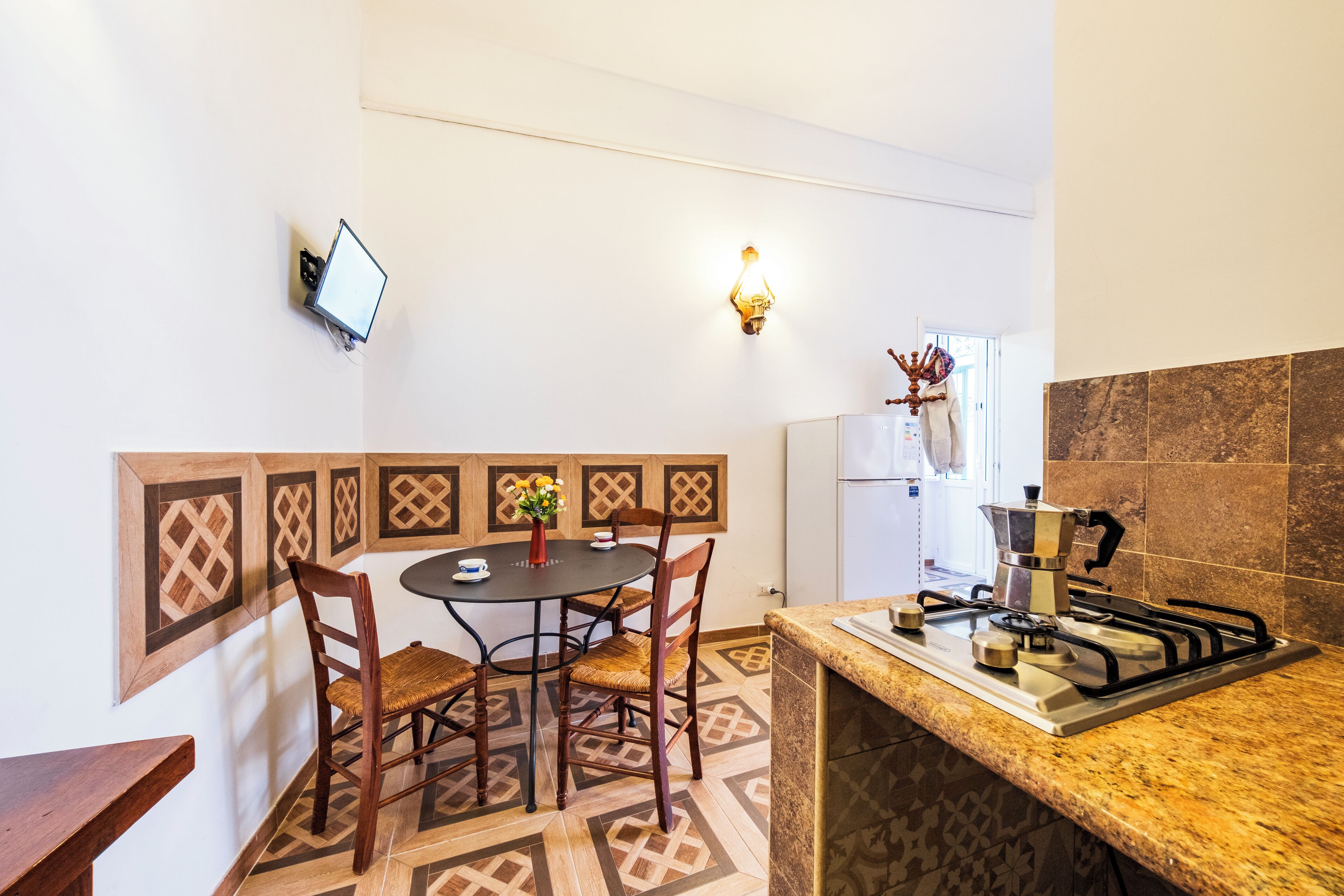 Cocina compacta con comedor, que incluye estufa a gas, una mesa pequeña con sillas y televisor montado en la pared.