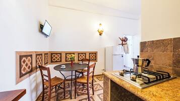 Cocina compacta con comedor, que incluye estufa a gas, una mesa pequeña con sillas y televisor montado en la pared.