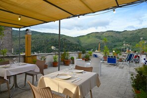An outdoor patio with tables and chairs, potted plants, and a view of green hills. - Affittacamere Al Seminario (Tivoli)