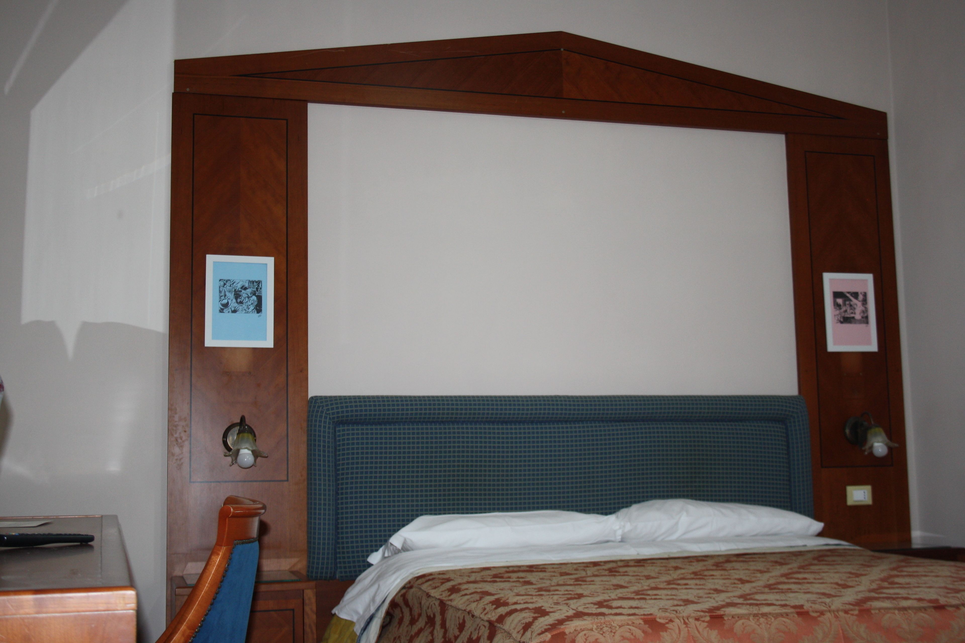 Een hotelkamer met een groot bed, een houten hoofdbord en twee ingelijste foto's aan de muur.