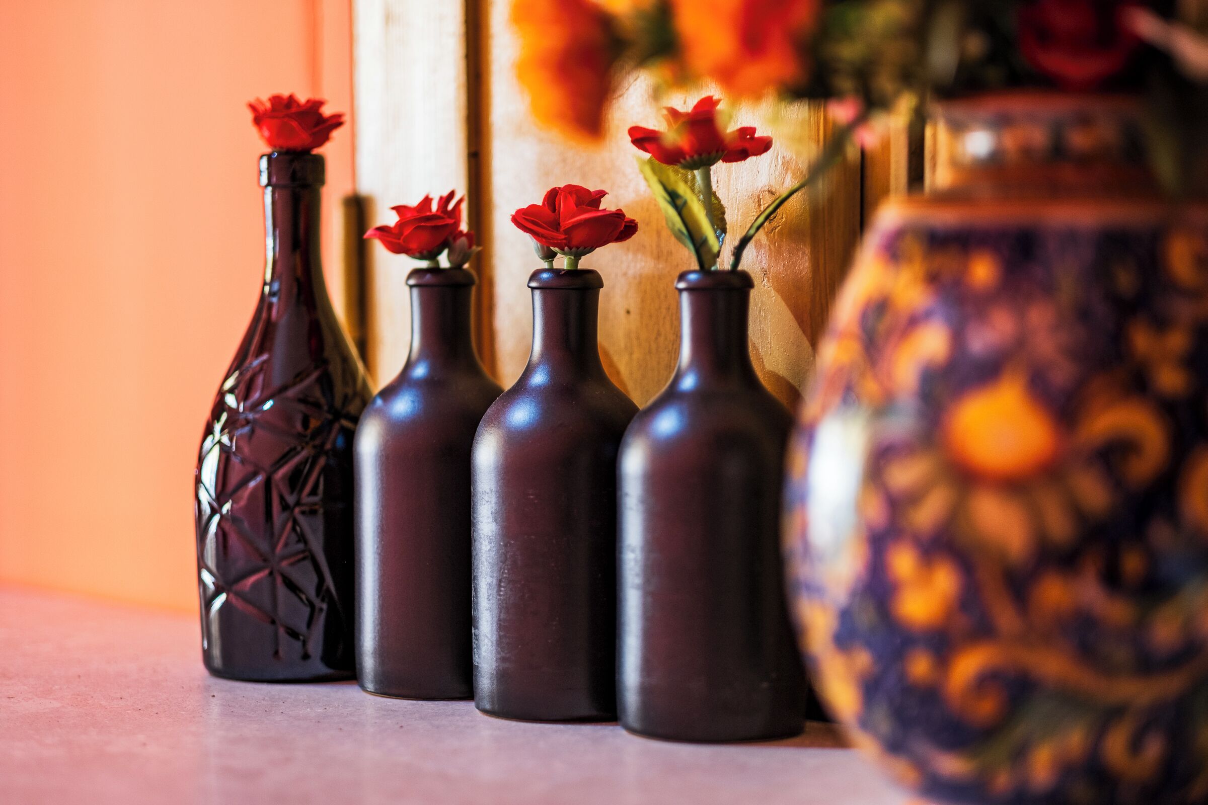 Four dark-colored vases with red roses on a table.