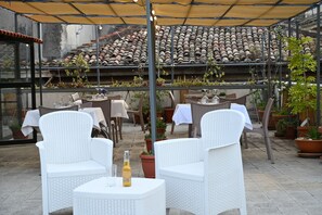 An outdoor patio with white wicker furniture, potted plants, and a tiled roof in the background. - Affittacamere Al Seminario (Tivoli)