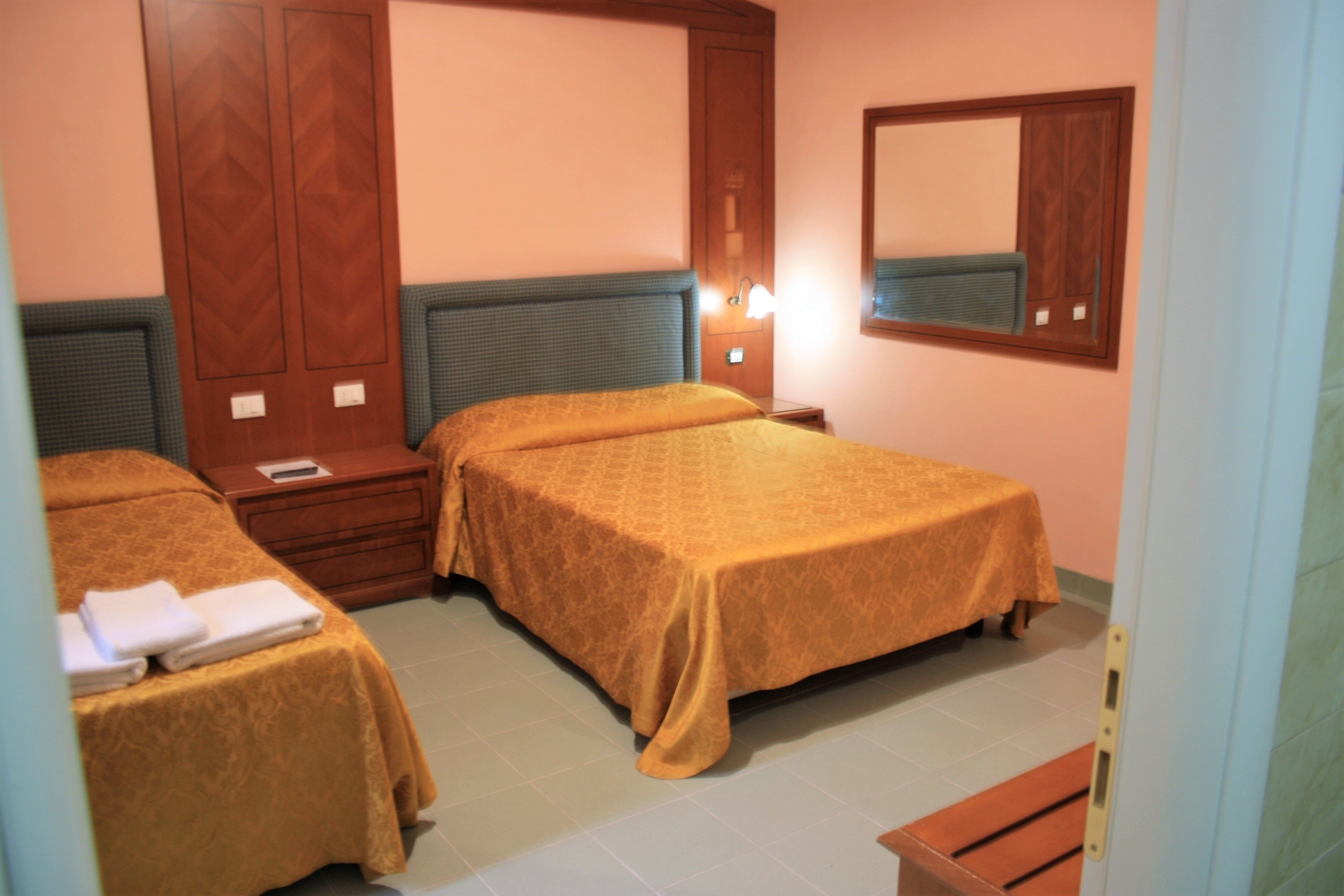 A hotel room with two beds, a wooden wardrobe, a nightstand, and a mirror on the wall.