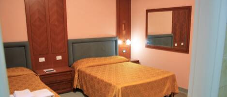 A hotel room with two beds, a wooden wardrobe, a nightstand, and a mirror on the wall.
