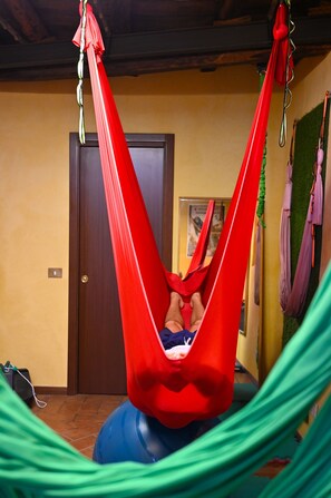 A hammock suspended from the ceiling in a room with a wooden door and a framed picture on the wall. - Affittacamere Al Seminario (Tivoli)