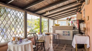 A cozy restaurant with a rustic wooden ceiling, large windows offering a view of greenery, and a tiled kitchen area. - Affittacamere Al Seminario (Tivoli)