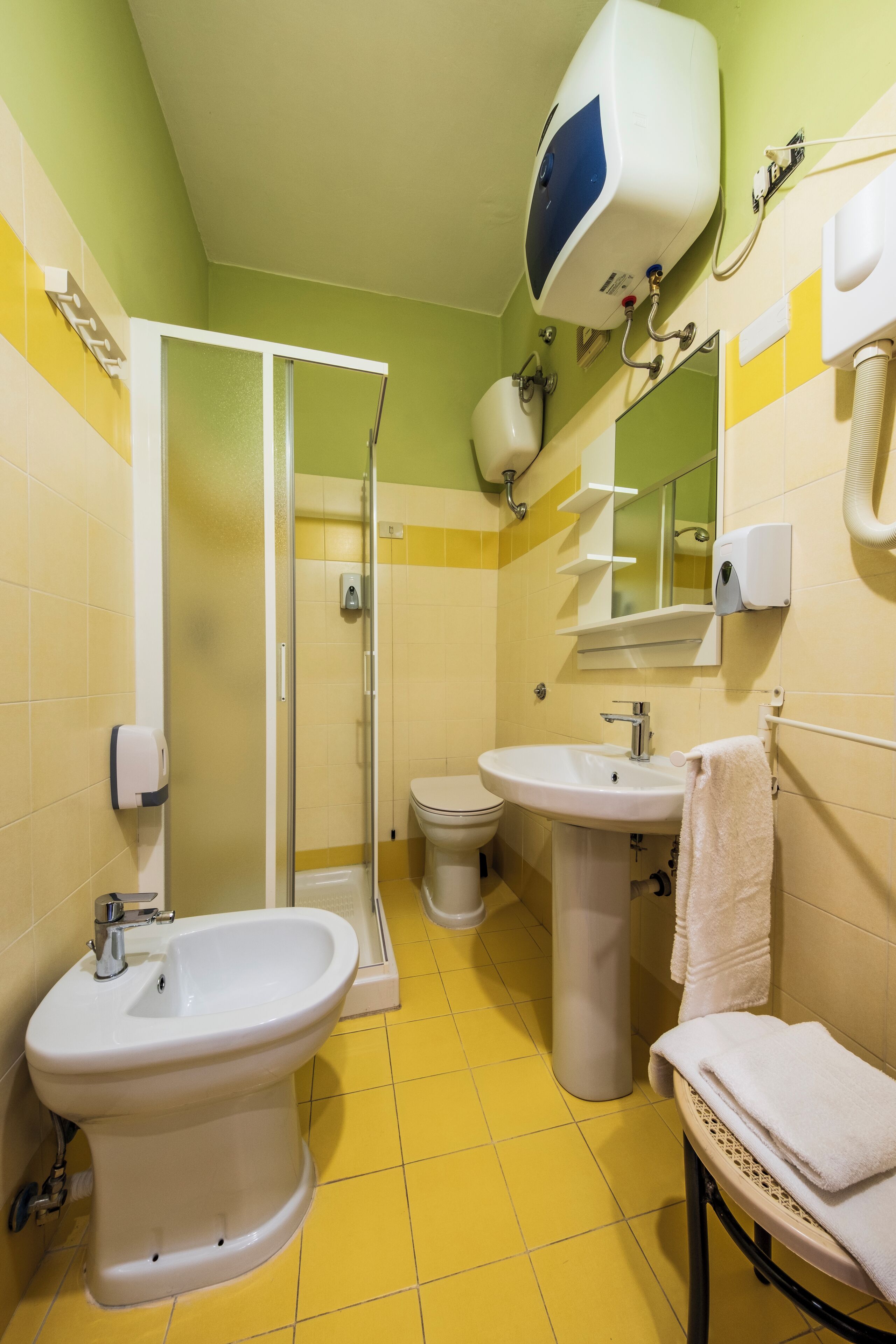Ein Badezimmer mit gelben und weißen Fliesen, einem Bidet, einer Toilette, einem Waschbecken und einem Handtuchhalter.