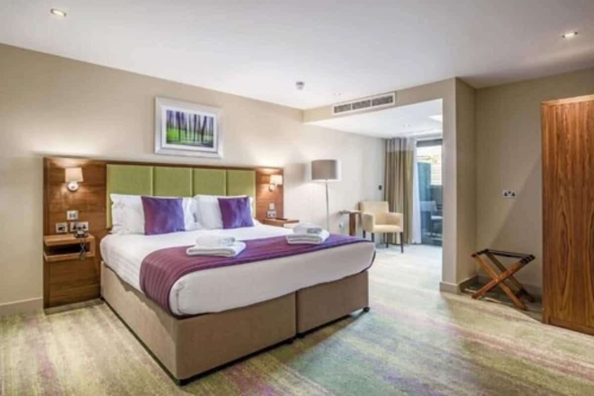 Une chambre d’hôtel avec un grand lit, une table de chevet, une lampe et une vue sur l’extérieur.