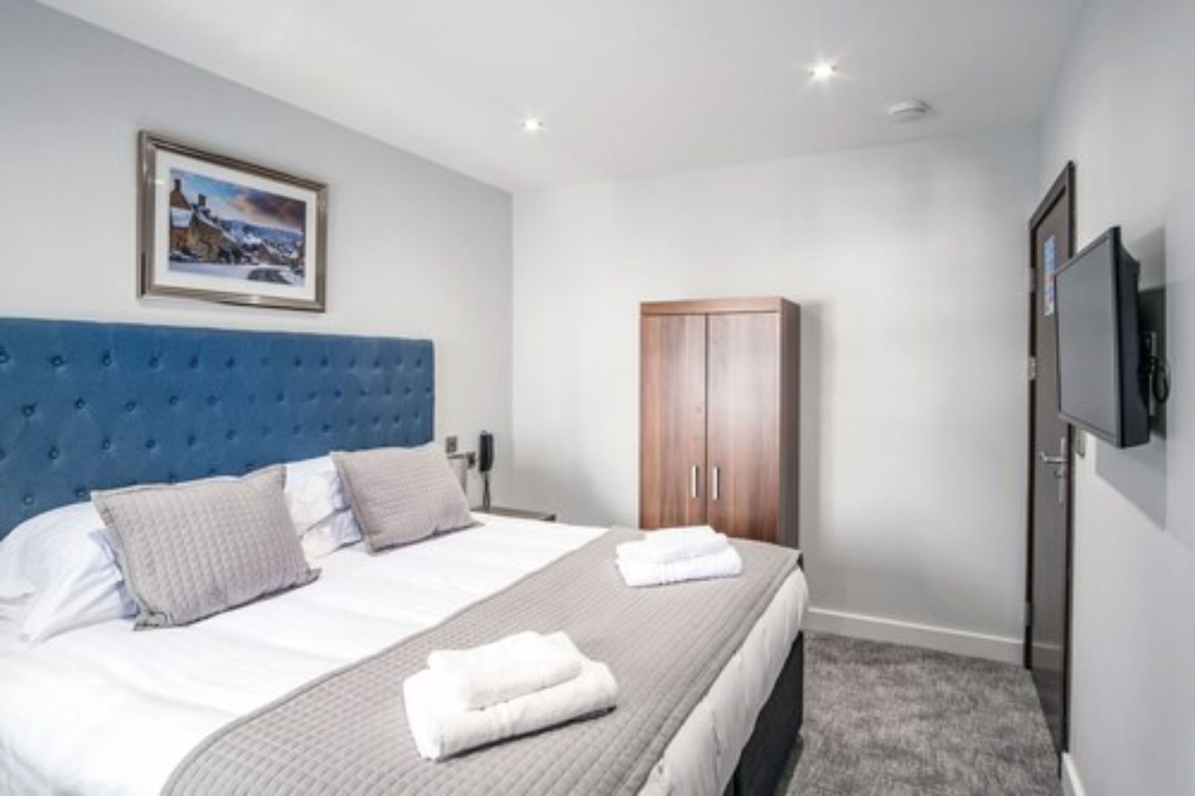 A hotel room with a large bed, a wooden wardrobe, a television, and a framed picture on the wall.