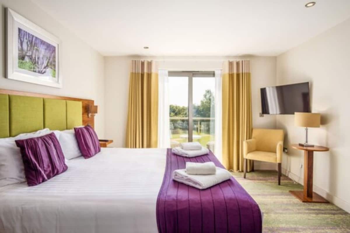 Une chambre d’hôtel avec un lit, une chaise, une télévision et une fenêtre avec des rideaux.