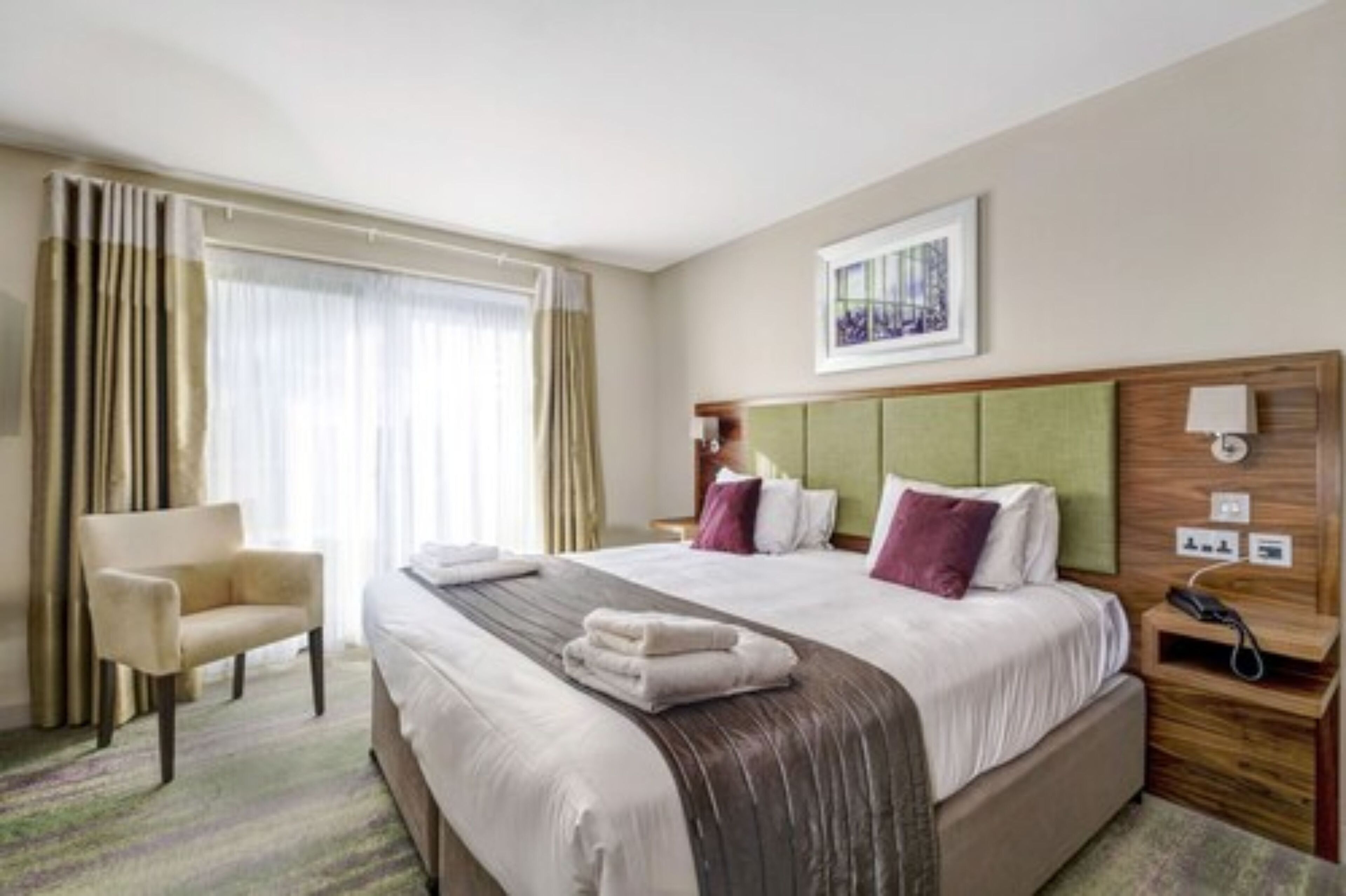 Une chambre d’hôtel avec un grand lit, une chaise, une table de chevet et une fenêtre avec des rideaux.